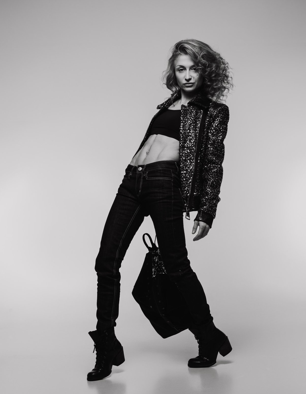 Girl with Blond Hair in a Black Jacket and Jeans of an Athletic Build Posing on a White Background, Black and White Image